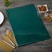 A green Hamilton menu board on a table with a fork and knife.