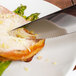 A Walco stainless steel steak knife cutting a piece of meat with asparagus on a plate.