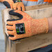 A person wearing Cordova orange heavy duty work gloves with black sandy nitrile palms holding a piece of wood.