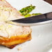 A Walco stainless steel steak knife with a brown Pakka wood handle cutting a piece of meat on a plate.