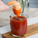 A hand holding a shrimp with a toothpick over a glass of red sauce in an Acopa round glass sauce cup.