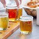 A person holding a tray of Acopa round glass sauce cups filled with beer.