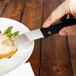 A person using a Walco steak knife to cut meat on a plate.