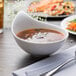 A Villeroy & Boch white porcelain bowl of soup with a spoon and fork on a table.