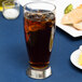 An Anchor Hocking Solace Cooler glass of brown liquid with ice on a blue table.