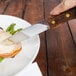A person holding a Walco steak knife to cut meat on a plate with vegetables.