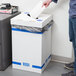 A person putting a piece of paper into a white Lavex Recycling Container lid.