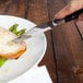 A person using a Walco Parisian steak knife to cut a piece of meat on a plate.