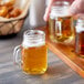 A person holding an Acopa mini mason jar mug filled with a liquid.