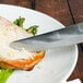 A Walco Boston Chop steak knife cutting food on a plate.