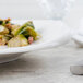 A Villeroy & Boch white porcelain flat plate with brussels sprouts and bacon on a table.