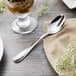A Walco Lancer stainless steel dessert spoon on a napkin next to a glass of milk.