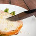 A Walco steak knife with a Pakka wood handle cutting a piece of meat on a plate.