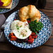 A plate with a breakfast sandwich, croissant, and a fork on it.