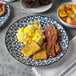 An Arcoroc Candour Azure porcelain dinner plate with eggs, bacon, and fruit on a table.