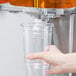 A hand holding a plastic cup under a Crathco beverage dispenser bowl.