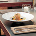 A close-up of food in a Villeroy & Boch white porcelain pasta bowl on a table with a white plate and silverware.