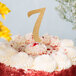 A close up of a white frosted cake with a gold glitter "7" on top.