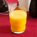 A Libbey beverage glass filled with orange juice on a red table.