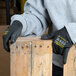 A person wearing Cordova Monarch black cut resistant gloves with black polyurethane palm coating holding a piece of wood.