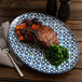 An Arcoroc Candour Azure porcelain oval platter with food on a table.