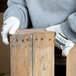 A pair of white cut resistant gloves with a white polyurethane palm coating being worn by a person handling wooden boards.