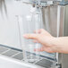 A person using a Crathco double beverage dispenser to fill a clear plastic cup.