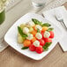 A white plastic salad plate with fruit and cheese on a table.