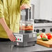 A person using a Robot Coupe commercial food processor on a counter to chop tomatoes and onions.