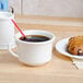 A white Tuxton china cup of coffee and a pastry on a table.