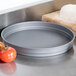 An American Metalcraft hard coat anodized aluminum cake pan on a counter next to tomatoes.