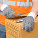 A person wearing Cordova natural polyester/cotton work gloves with black PVC dots on the palms holding a box.