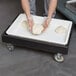 A person using the Cambro Black Pizza Dough Box Camdolly to hold dough.