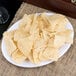 A Carlisle white oval melamine platter with a plate of chips on a table.