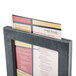 A Menu Solutions ash wood menu tent in a black frame holding a menu.