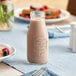 An Acopa glass milk bottle on a table with a bowl of cereal and fruit.