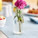 An Acopa glass milk bottle with flowers on a table.