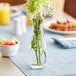 An Acopa glass milk bottle filled with flowers on a table.