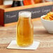 A close up of an Acopa glass milk bottle filled with liquid on a coaster.