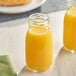 Two Acopa glass milk bottles filled with yellow liquid on a table.