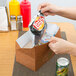 A person putting food into a red Hearthstone take-out box with a silver top.