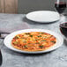 An American Metalcraft white ceramic pizza serving tray with a pizza on it next to a glass of wine.