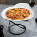 A white ceramic pizza serving tray with a pizza on it and a glass of wine on the table.