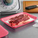 A CKF rose foam meat tray holding raw steaks on a counter.