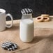 A black and white plaid lid on an Acopa milk bottle on a table with cookies.