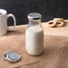 An Acopa silver lid on a glass bottle of milk on a table.