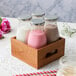 A wooden crate holding Acopa glass bottles of milk and pink liquid.