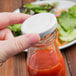 A person holding a white Acopa milk bottle lid over a bottle of sauce.