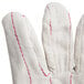 A close up of a Cordova Economy Weight Nap-In polyester / cotton double palm work glove with red stitching.