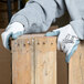 A person wearing Cordova white nylon gloves with gray foam nitrile palm coating holding a piece of wood.